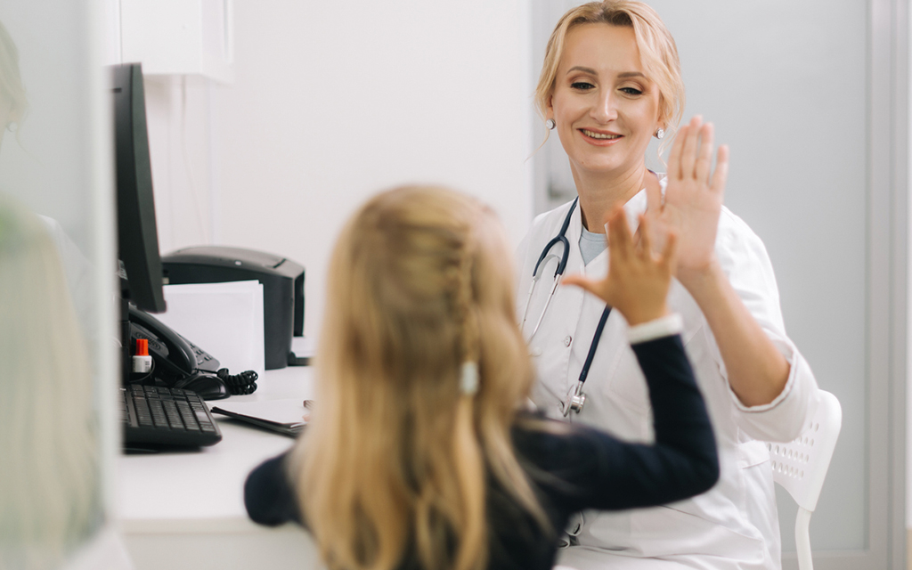 Young woman doctor pediatrician talking to little girl patient